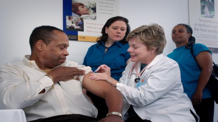 A doctor gives a patient a shot with two nurses watching.